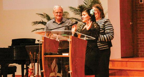 Michelle “Shelby” Muyango (center), joined by Pastor John Kent and Karen Schneider, shares her testimony.