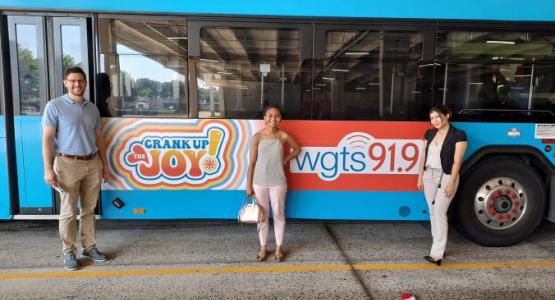 Leadership associates Thomas Ozio, Lindsey Gispert and Josseline Ayala stand in front of WGTS' bus advertisement. 