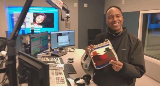 Morning show host Jerry Woods holds up a purse given to him by his sponsored child’s mom.