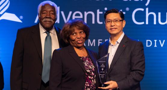 Sung Kwon presents an award to Minnie McNeil as her husband, Andrew, looks on.