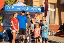 2.	Afternoon hosts, Johnny and Stacey Stone, pose with a family in front of the WGTS broadcast tent.