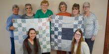 Lois Ruth (standing, second from right) and the Columbus Eastwood Women’s Ministries team hold two handmade quilts for infants at a local hospital.
